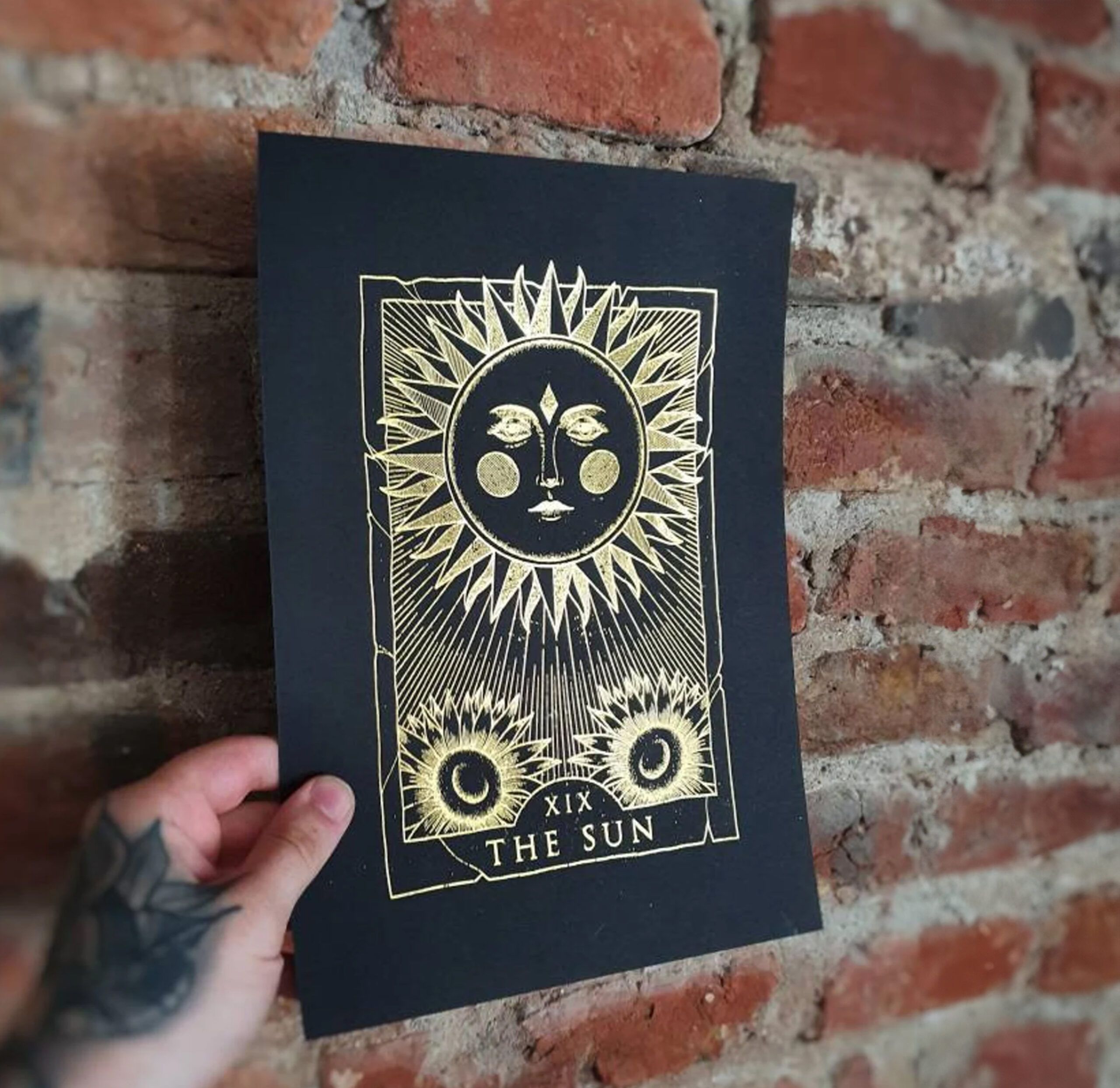 Gold metallic foil print with sun design and decorative elements on black card stock