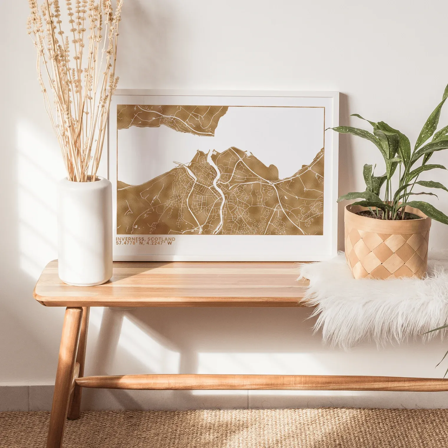 Gold metallic foil landscape print in a white frame on a wooden bench with plants in the background